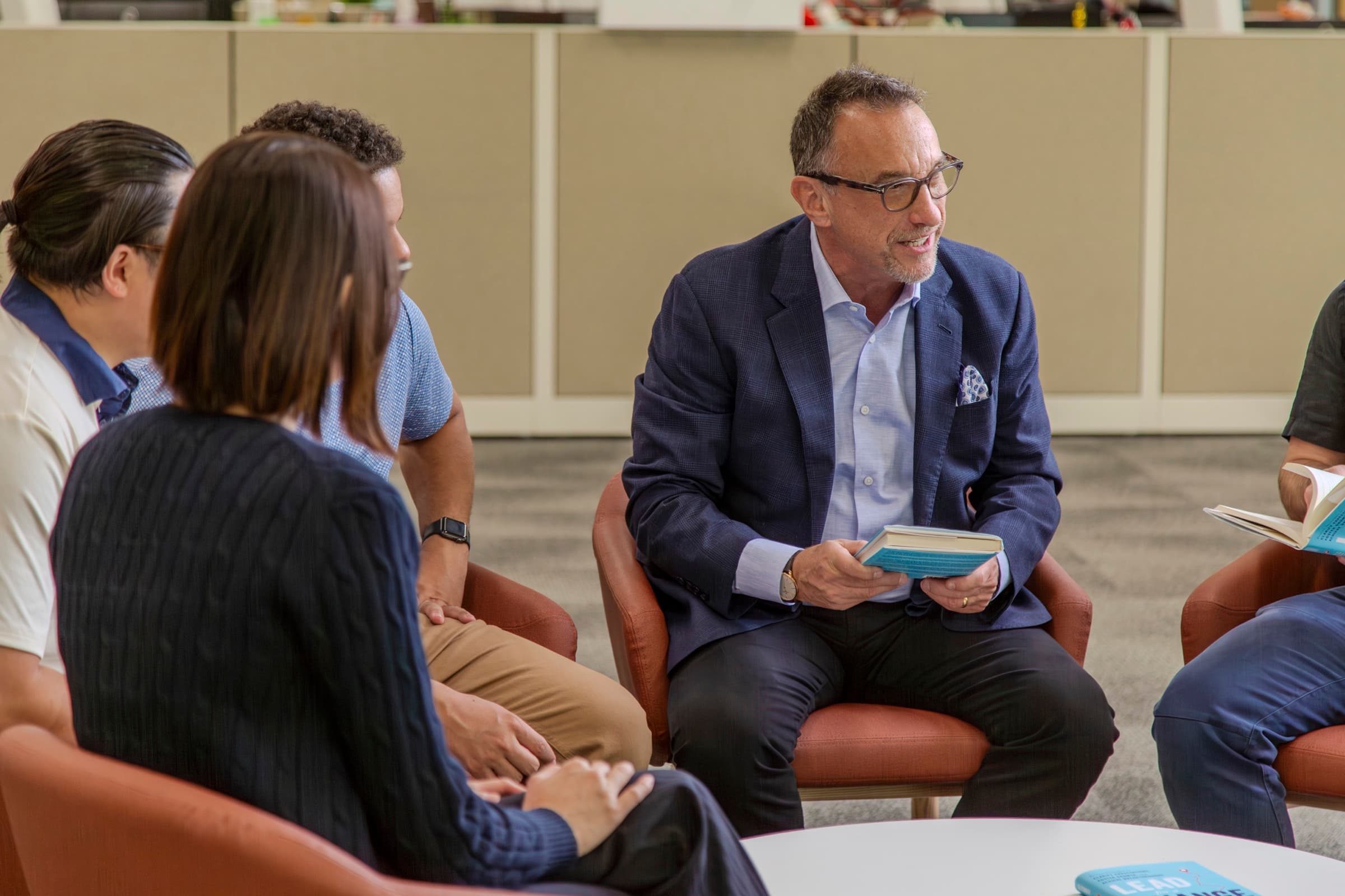 Ron Glickman leading a small cohort seated in a circle, a copy of Lead for a Change in hand.
