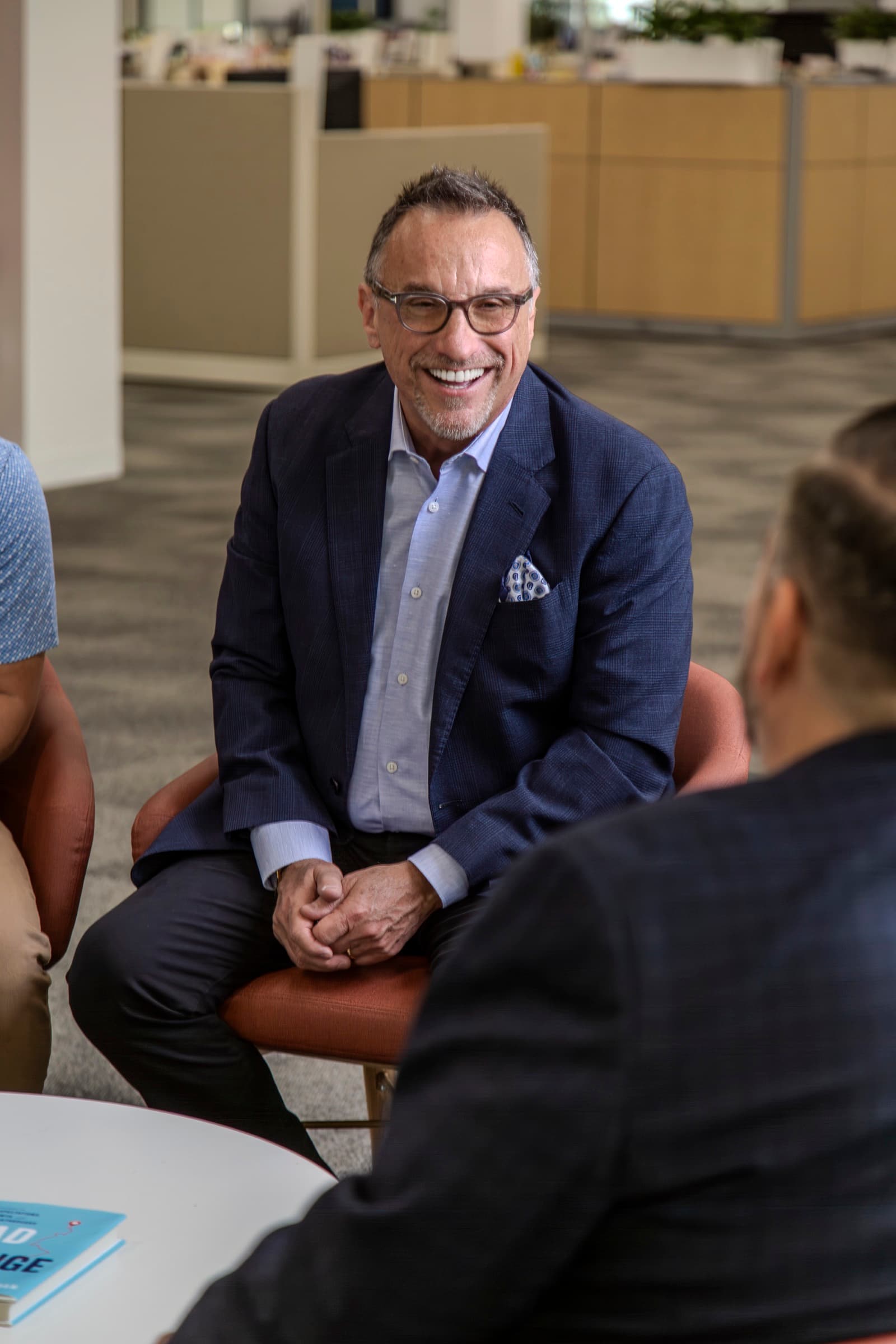 Ron Glickman seated across a small table from a coachee, listening, hands clasped.