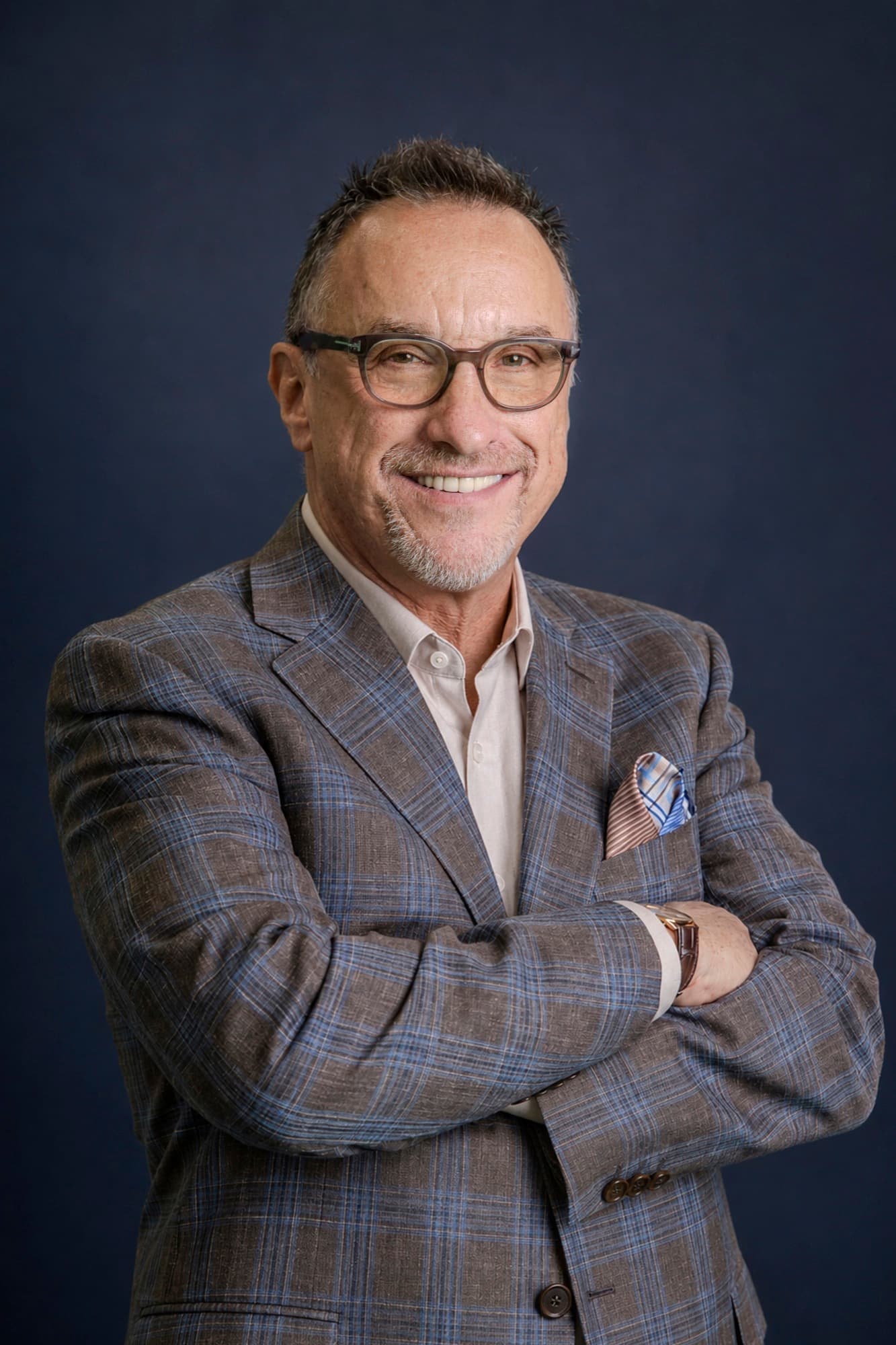 Dr. Ron Glickman, arms crossed, smiling, in a checked blazer against a navy backdrop.