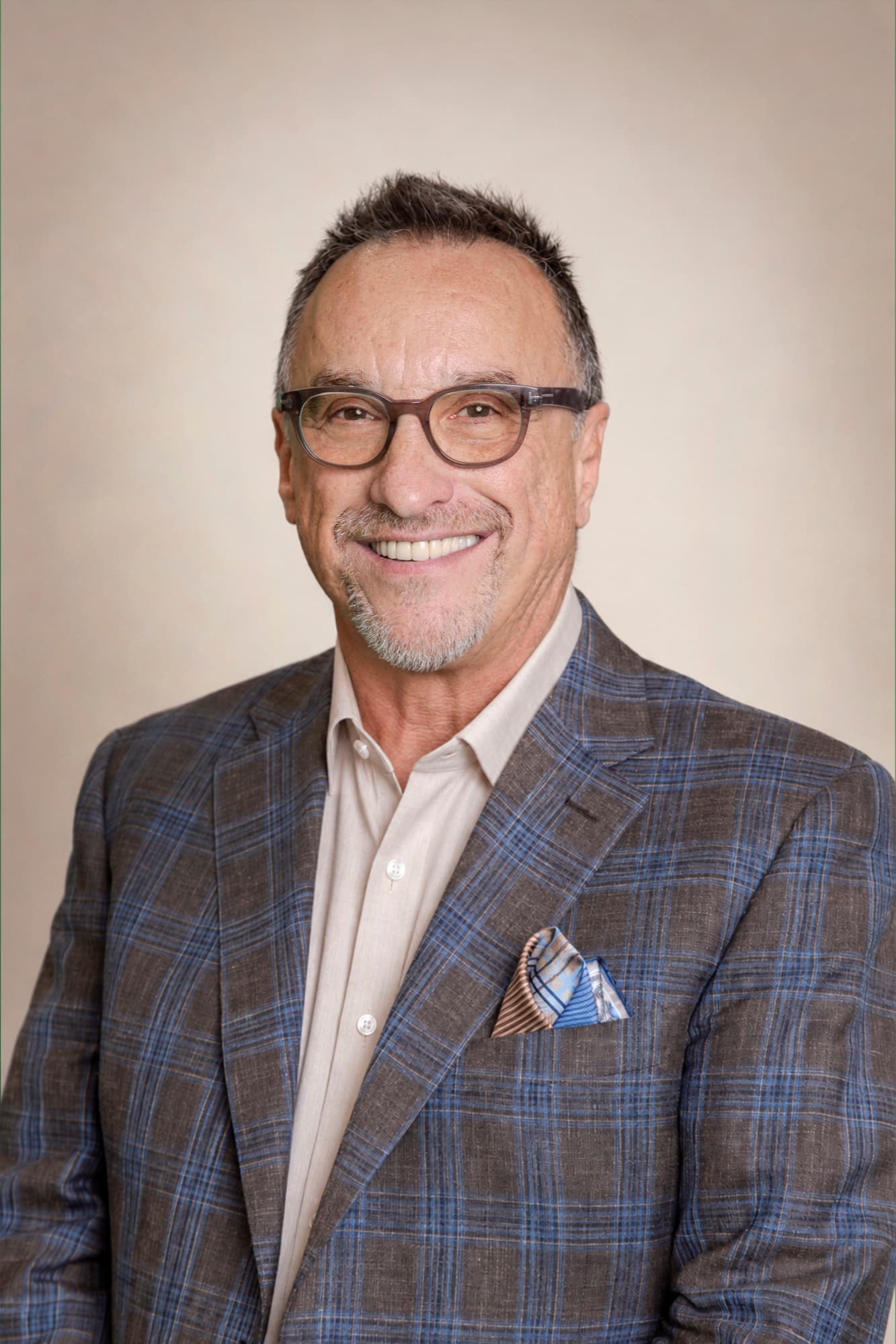 Dr. Ron Glickman — studio portrait in a checked blazer, smiling, on a warm light backdrop.